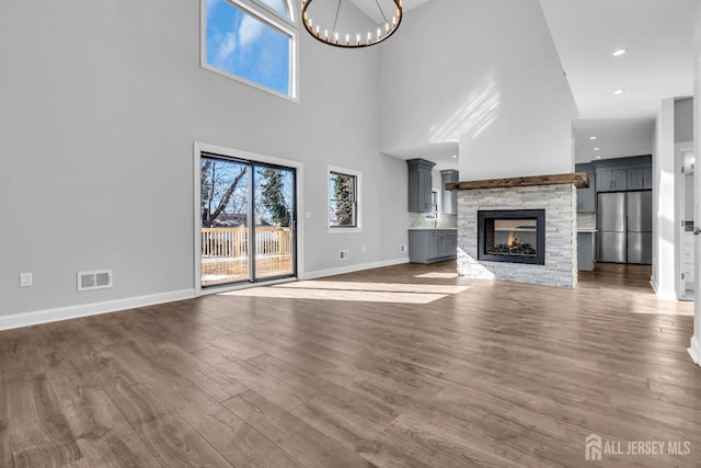 unfurnished living room featuring baseboards, visible vents, dark wood-style flooring, an inviting chandelier, and a stone fireplace