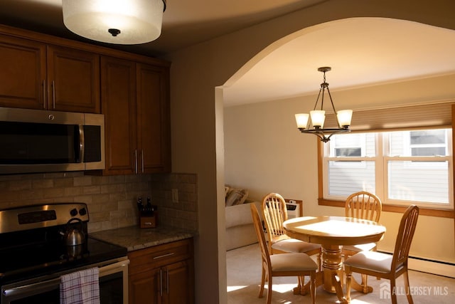 kitchen with an inviting chandelier, arched walkways, light stone counters, stainless steel appliances, and decorative backsplash