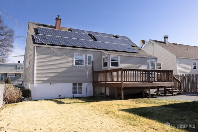 rear view of property featuring a lawn, fence, solar panels, a chimney, and a deck