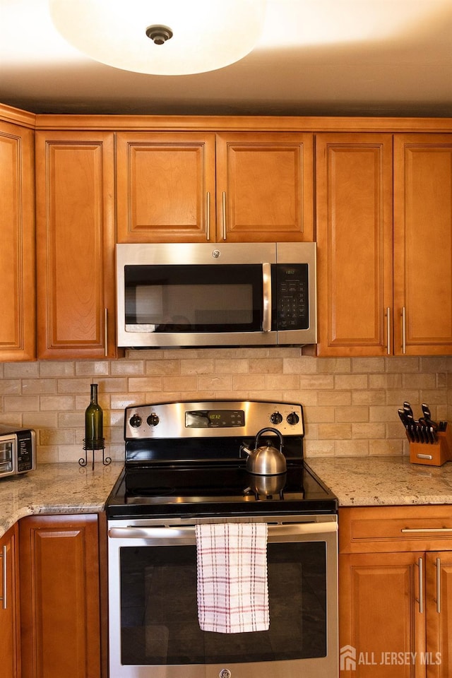 kitchen featuring brown cabinetry, decorative backsplash, appliances with stainless steel finishes, and light stone countertops