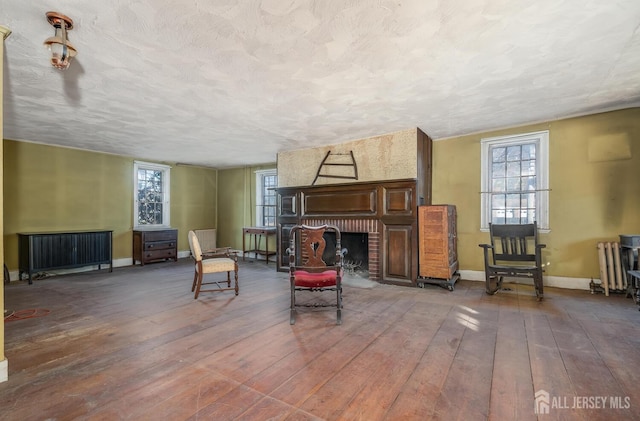 living area with a brick fireplace, a textured ceiling, radiator, and wood-type flooring