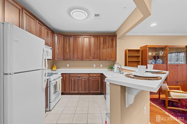 kitchen featuring light tile patterned floors, kitchen peninsula, white appliances, a breakfast bar, and sink