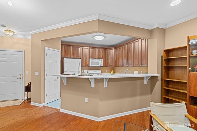 kitchen with white appliances, light hardwood / wood-style floors, kitchen peninsula, a breakfast bar, and crown molding