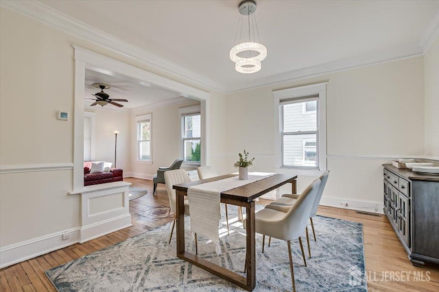 dining space featuring ornamental molding, ceiling fan with notable chandelier, and light wood-type flooring