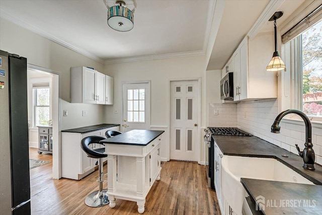 kitchen with sink, stainless steel appliances, a kitchen island, hardwood / wood-style floors, and white cabinets