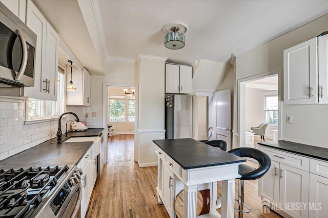 kitchen with light wood-type flooring, stainless steel appliances, sink, decorative light fixtures, and white cabinetry