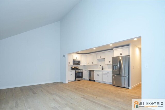 kitchen featuring appliances with stainless steel finishes, sink, high vaulted ceiling, light hardwood / wood-style floors, and white cabinetry