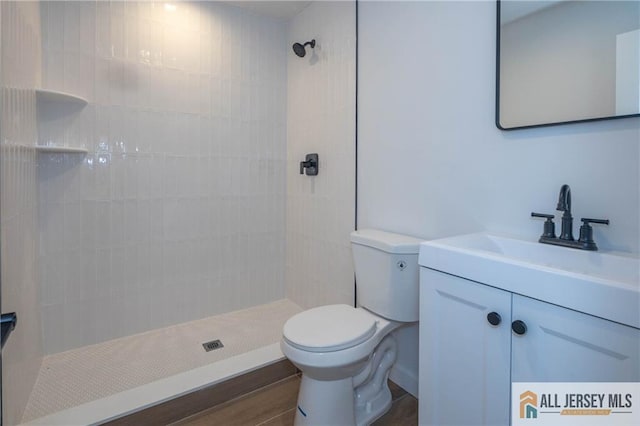 bathroom with tiled shower, wood-type flooring, vanity, and toilet