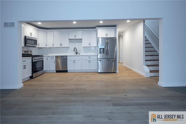 kitchen with light wood-type flooring, stainless steel appliances, white cabinetry, and sink