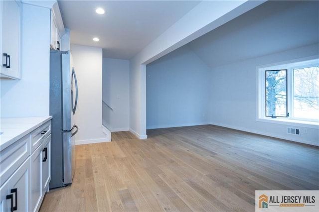 kitchen featuring white cabinetry, stainless steel fridge, light stone counters, and light wood-type flooring