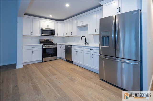 kitchen featuring appliances with stainless steel finishes, light hardwood / wood-style floors, white cabinetry, and sink