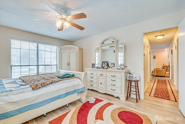 bedroom with light wood-type flooring, ceiling fan, and a textured ceiling