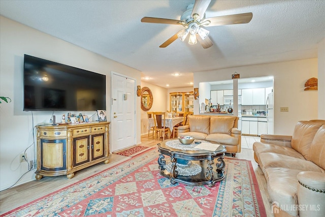 living area with a ceiling fan, light wood-type flooring, and a textured ceiling