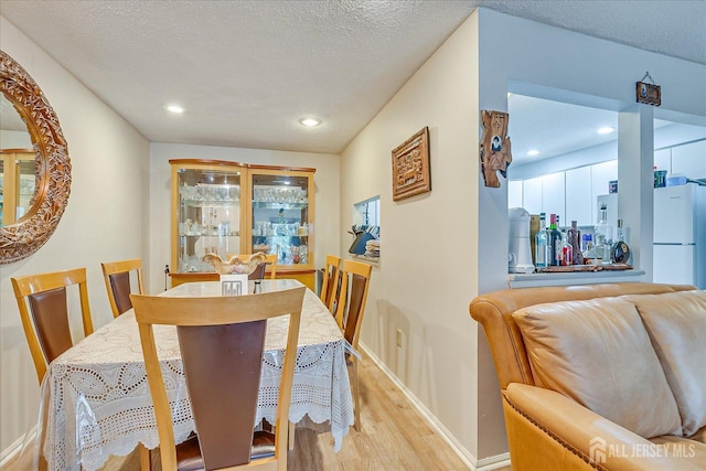 dining area featuring light wood-type flooring, a textured ceiling, baseboards, and recessed lighting