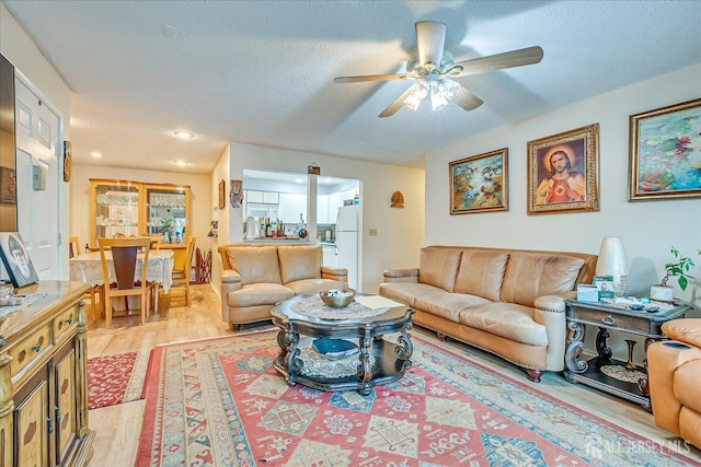 living area featuring a textured ceiling, a ceiling fan, and light wood-style floors