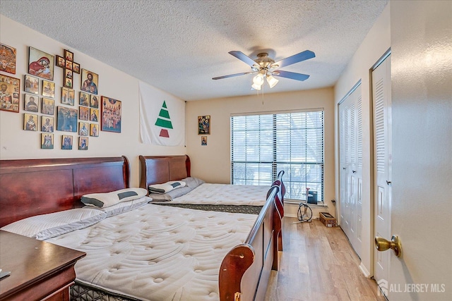 bedroom with light wood-style floors, ceiling fan, a textured ceiling, and multiple closets