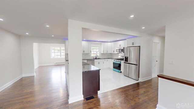 kitchen with decorative backsplash, appliances with stainless steel finishes, light wood-type flooring, dark stone counters, and white cabinets