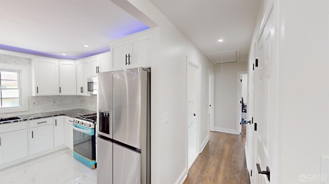 kitchen with hardwood / wood-style floors, backsplash, white cabinets, dark stone countertops, and stainless steel appliances