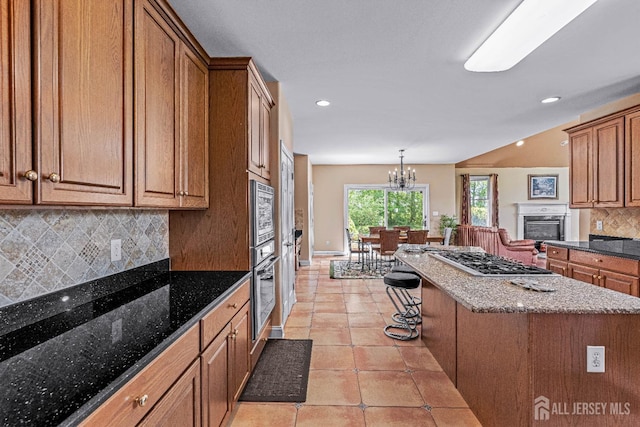 9 Narrow Brook Ct, Plainsboro, NJ 08536 - kitchen featuring appliances with stainless steel finishes, a glass covered fireplace, brown cabinets, tasteful backsplash, and a kitchen island