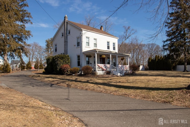 view of front facade featuring covered porch, a chimney, and a front lawn