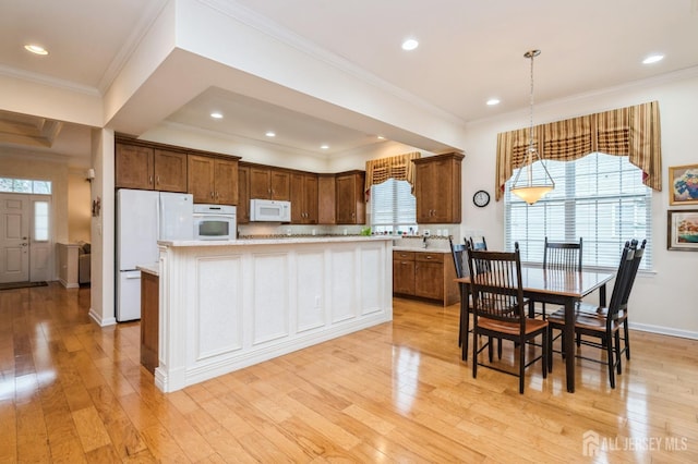 kitchen with white appliances, a center island, hanging light fixtures, and light wood-type flooring