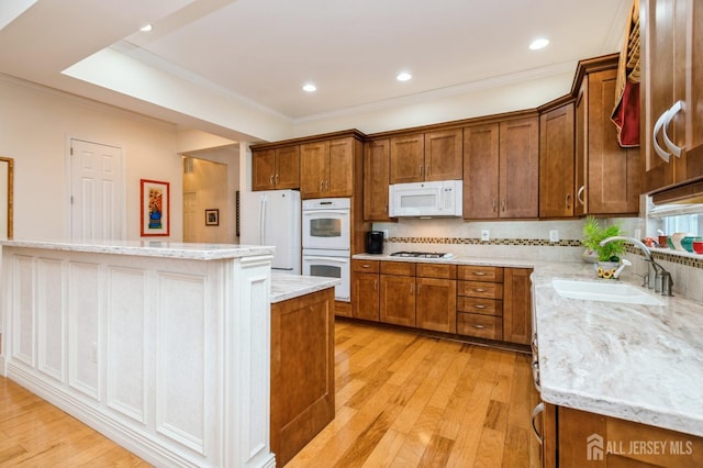 kitchen with light wood-type flooring, a kitchen island, light stone countertops, sink, and white appliances