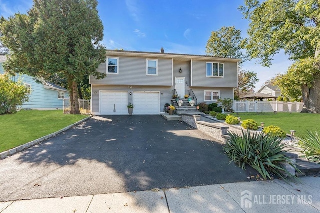 raised ranch featuring a garage, driveway, a front lawn, and fence