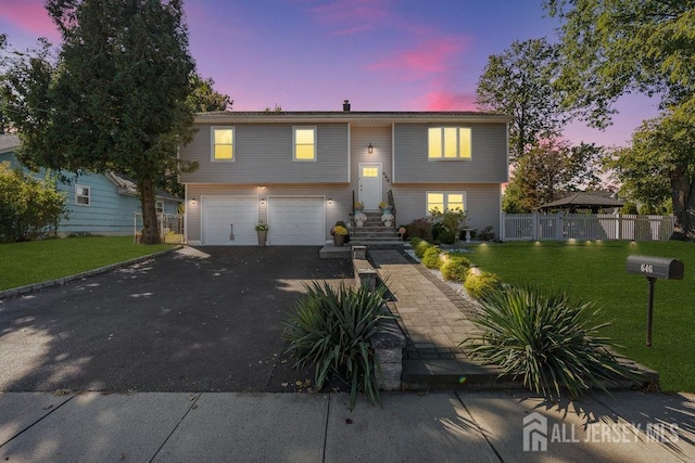 raised ranch featuring a front yard, an attached garage, fence, and driveway