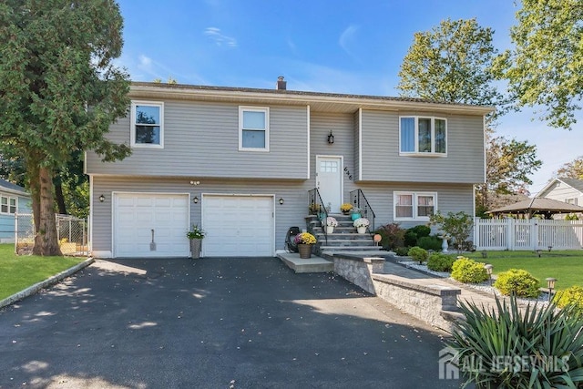 split foyer home featuring aphalt driveway, a garage, a front lawn, and fence