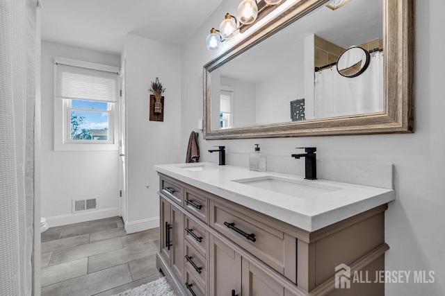 bathroom with double vanity, visible vents, baseboards, and a sink