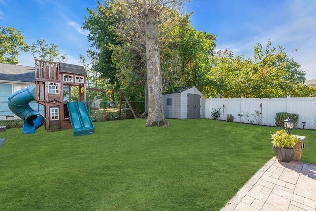 view of yard featuring a storage shed, an outbuilding, a playground, and a fenced backyard