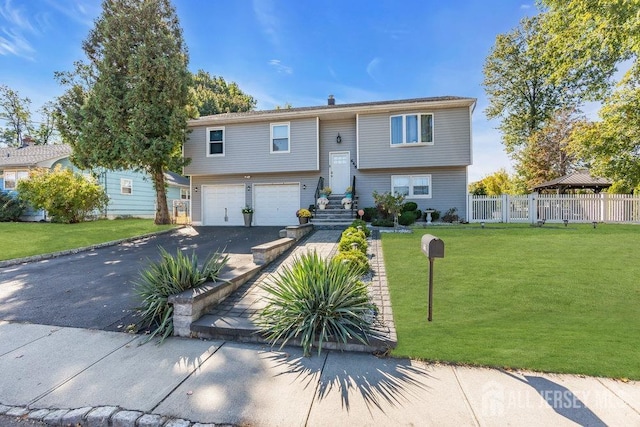 bi-level home with aphalt driveway, fence, a garage, and a front yard