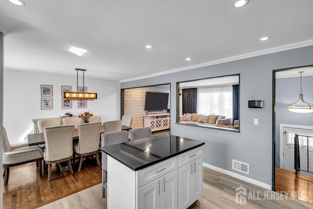 kitchen with white cabinetry, visible vents, light wood finished floors, and ornamental molding