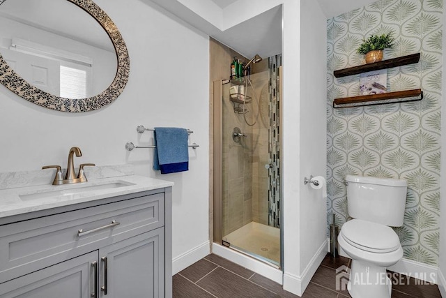 bathroom with a shower stall, wallpapered walls, baseboards, toilet, and vanity