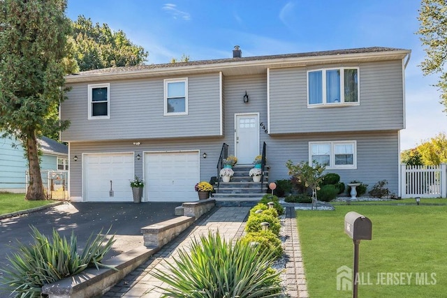 raised ranch featuring a front yard, fence, an attached garage, a chimney, and aphalt driveway