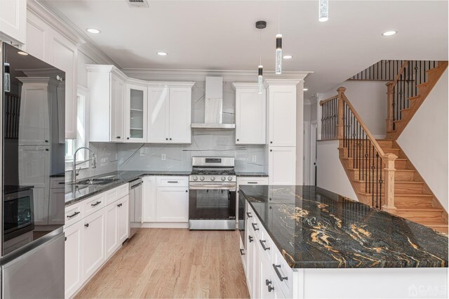 kitchen featuring appliances with stainless steel finishes, tasteful backsplash, white cabinetry, light wood-type flooring, and wall chimney exhaust hood