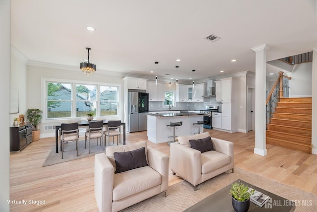 living room with decorative columns, sink, ornamental molding, a notable chandelier, and light hardwood / wood-style flooring