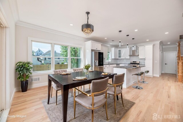 dining space with crown molding, sink, an inviting chandelier, and light wood-type flooring