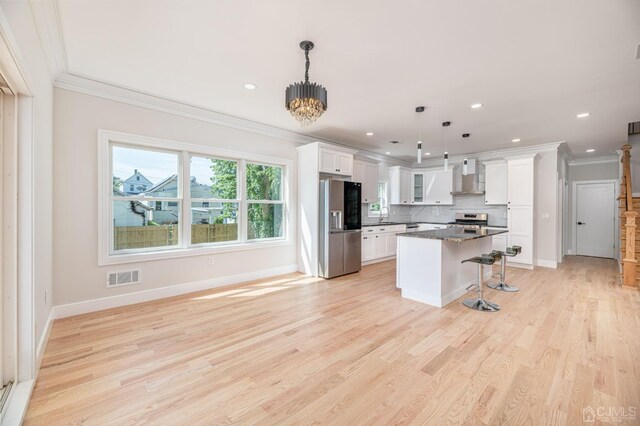 kitchen featuring white cabinetry, wall chimney range hood, decorative light fixtures, and stainless steel appliances