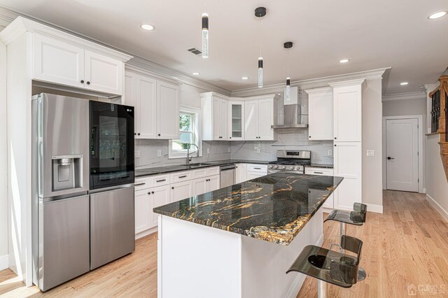 kitchen with pendant lighting, sink, stainless steel appliances, a kitchen island, and wall chimney exhaust hood