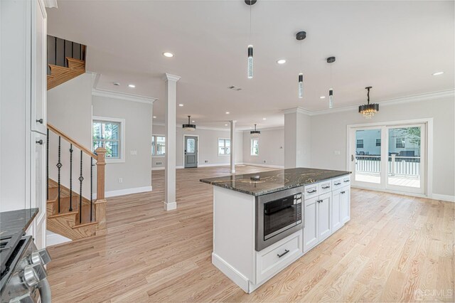 kitchen featuring pendant lighting, stove, dark stone countertops, stainless steel microwave, and white cabinets