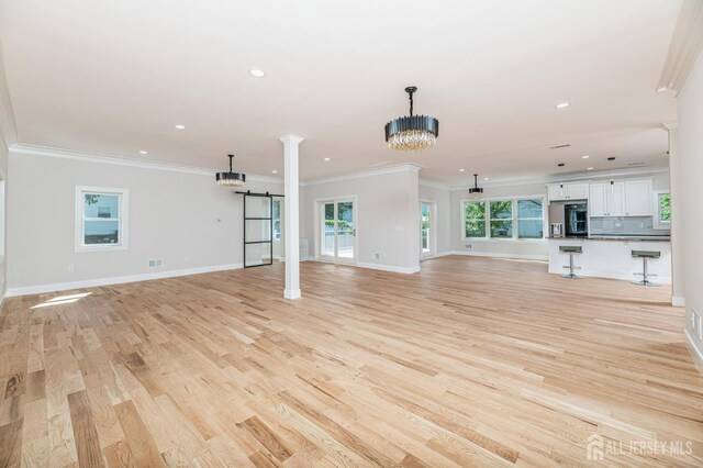 unfurnished living room with an inviting chandelier, ornamental molding, a barn door, and light wood-type flooring