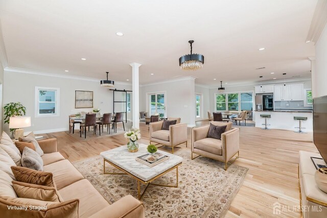 living room featuring ornate columns, crown molding, an inviting chandelier, and light hardwood / wood-style floors