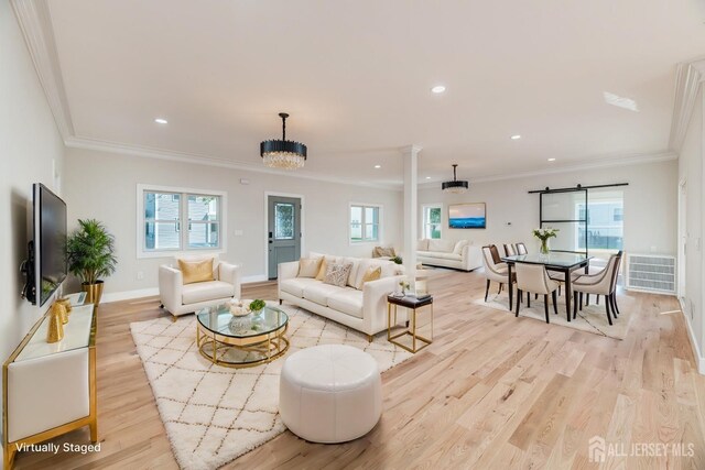 living room featuring crown molding, a notable chandelier, ornate columns, and light wood-type flooring