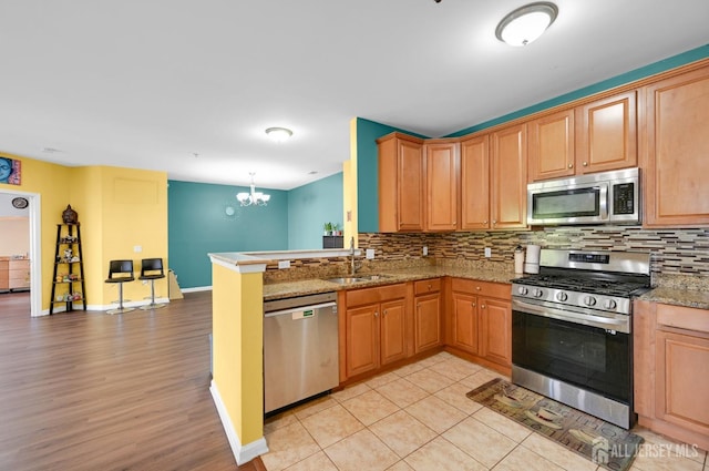 kitchen with appliances with stainless steel finishes, a sink, decorative backsplash, and a chandelier