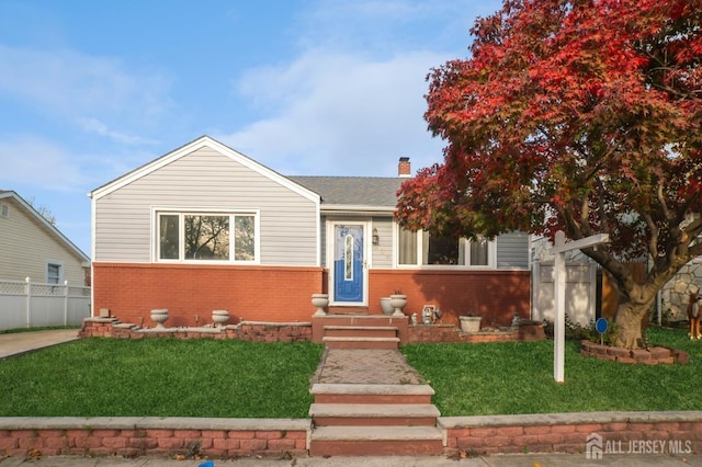 view of front of property with a front yard, a chimney, fence, and brick siding