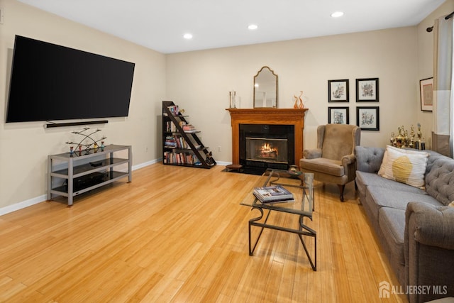 living room featuring baseboards, a warm lit fireplace, light wood finished floors, and recessed lighting