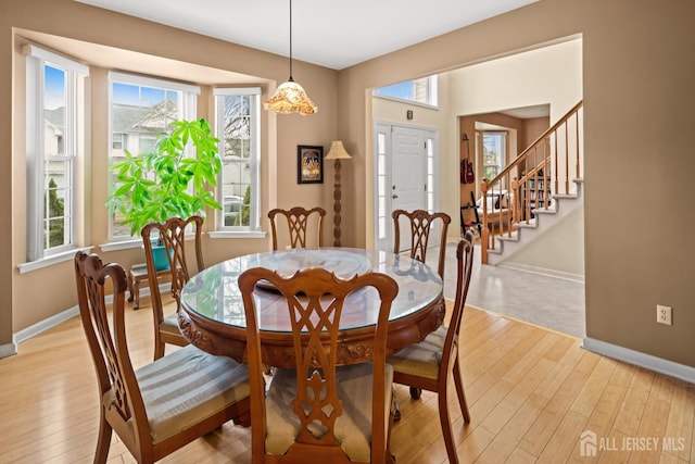 dining space featuring baseboards, light wood-style floors, and stairway