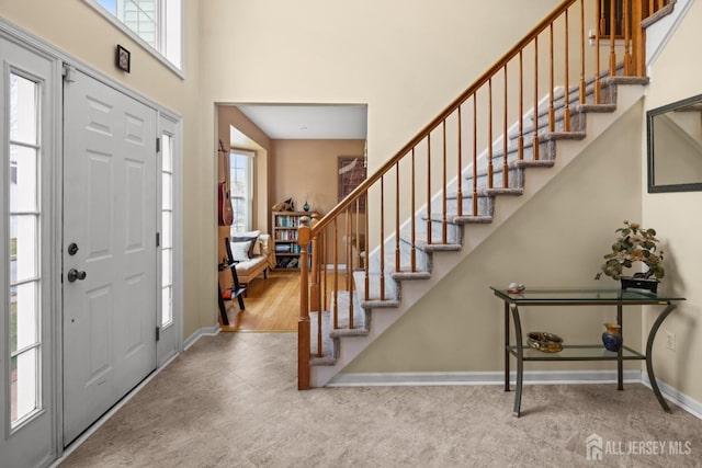 foyer entrance with a towering ceiling, baseboards, and stairs