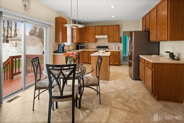 kitchen featuring under cabinet range hood, stainless steel appliances, light countertops, visible vents, and brown cabinetry